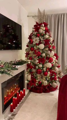 a christmas tree decorated with red and white ornaments in front of a fire place filled with candles