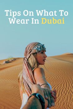 a man and woman holding hands in the desert with text that reads tips on what to wear in dubai