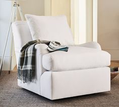 a white chair with a blanket on it in a living room next to a lamp