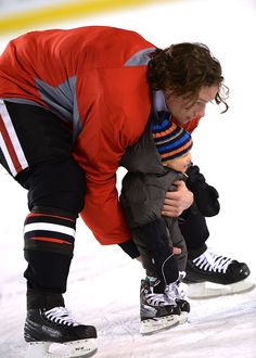 a man holding a small child on top of a skateboard in an ice rink