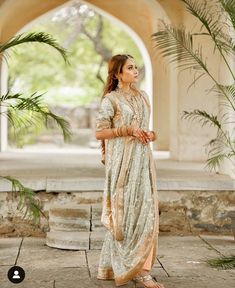 a woman standing in front of an archway wearing a white and gold outfit with palm trees