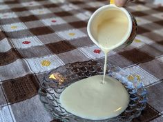 a person pouring milk into a glass bowl on a checkered tablecloth covered table