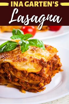 two white plates with lasagna on them and tomatoes, basil leaves, and cherry tomatoes in the background