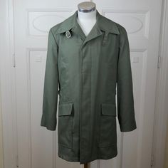 This 1990s European vintage olive green jacket has a wide wing collar that you can also turn up and buckle closed. The jacket has padded shoulders, closes in the front with five concealed buttons, and has a elasticated inner drawstring at the waist. A silicone finish on the outside of the jacket means that it is water-resistant. The jacket is lined in a gold satin polyester fabric. Note that this jacket originally had a hood attached by a zipper (under the collar), but the hood is no longer avai Military Style Green Long Coat, Fitted Green Military Outerwear, Vintage Khaki Outerwear With Lapel Collar, Vintage Outerwear With Lapel Collar, Vintage Double-breasted Solid Outerwear, Vintage Olive Outerwear With Buttons, Vintage Khaki Outerwear For Formal Occasions, Green Long Sleeve Uniform Outerwear, Retro Green Formal Outerwear