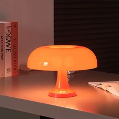 an orange table lamp sitting on top of a desk next to a book and some books