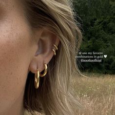 a close up of a person wearing large gold hoop earrings with trees in the background