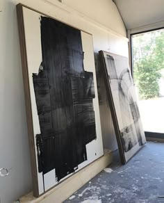 two black and white paintings are on display in an empty room next to a window