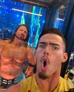 two men with their mouths open standing in front of a large screen at a wrestling match