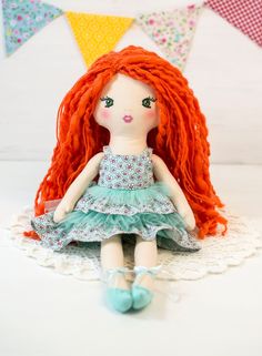 a red haired doll sitting on top of a doily with bunting around it