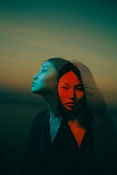 two women standing next to each other in front of the ocean at sunset or sunrise