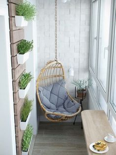 a small balcony with a hanging chair, table and potted plants on the wall