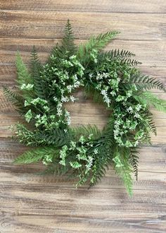 a green wreath with white flowers on a wooden surface