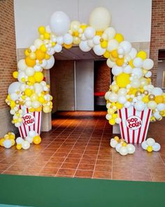 an arch made out of balloons and popcorn buckets is decorated with yellow and white balloons