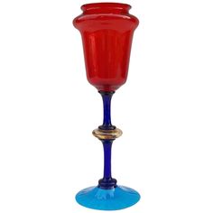 a red and blue wine glass sitting on top of a blue base with a gold rim