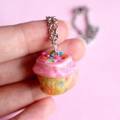 a tiny pink cupcake necklace with sprinkles on it