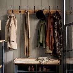 a coat rack filled with coats and shoes next to a wooden bench in a room