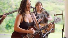 a woman singing into a microphone while holding an acoustic guitar in front of two other people