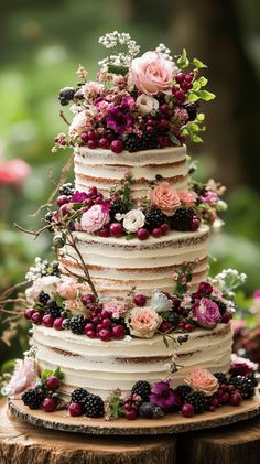 a multi layer cake with flowers and berries on top is sitting on a tree stump