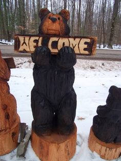 three carved bears holding a welcome sign in front of snow covered ground with trees behind them