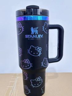 a black travel mug with hello kitty images on the front and side, sitting on a table