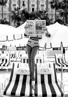 a woman standing on top of two lounge chairs while holding a newspaper in her hand