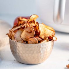 a silver bowl filled with chips on top of a table next to an apple and other food items