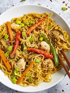 a white bowl filled with noodles, chicken and veggies next to chopsticks