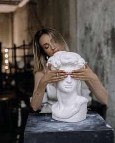 a woman covering her face behind a white busturizer sculpture in a room filled with tables and chairs