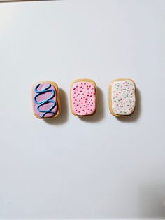 three decorated cookies sitting on top of a white table next to each other with frosting and sprinkles