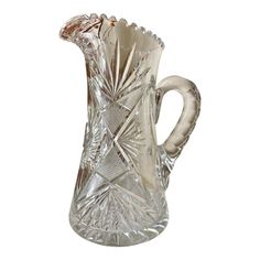 a clear glass pitcher with an intricate design on the front and sides, set against a white background