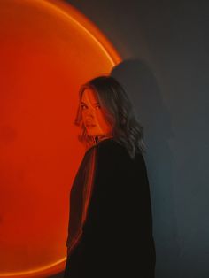 a woman is standing in front of an orange circle with her head turned to the side