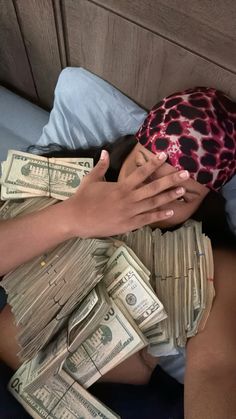 a woman laying in bed with stacks of money on top of her head and hands covering her face