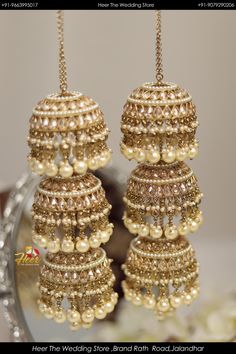 two golden bells with pearls hanging from it's sides in front of a mirror