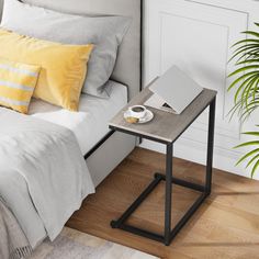 a small table with a laptop on it next to a bed and potted plant