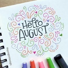 an open notebook with markers and pens next to it that says hello august on the page