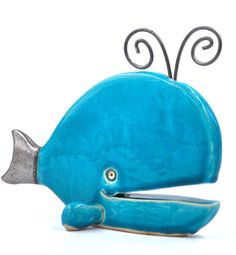 a blue ceramic whale sculpture with scissors in it's mouth, on a white background