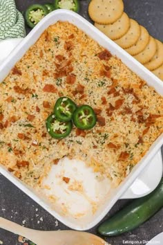 a casserole dish with cheese and green peppers on top next to crackers