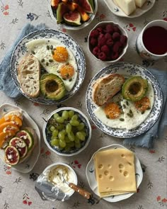 a table topped with plates of food next to bowls of fruit and crackers on top of a table