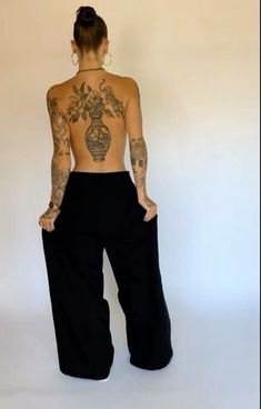 a woman with tattoos on her back standing in front of a white wall and wearing black pants