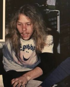 a man with long hair sitting in front of a laptop computer