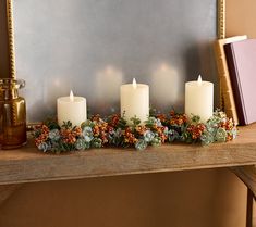 candles are arranged on a mantle with greenery