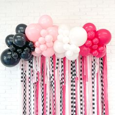 balloons and streamers are hanging on the wall in front of a brick wall with black and white stripes