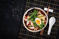 a bowl filled with noodles and vegetables next to chopsticks on top of a mat