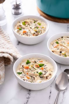 three white bowls filled with soup sitting on top of a counter next to spoons