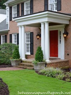 a red door is on the side of a brick house with white columns and black shutters