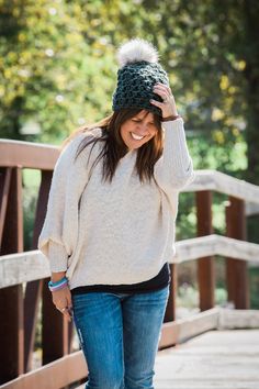 a woman walking across a bridge while wearing a knitted hat with pom - poms