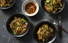 four bowls filled with noodles and vegetables on top of a gray table next to utensils