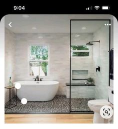 a white bath tub sitting next to a toilet under a window in a bathroom with wooden floors