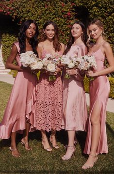 four bridesmaids in pink dresses posing for a photo with their bouquets on the grass