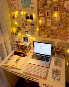 an open laptop computer sitting on top of a white desk next to a wall covered in pictures